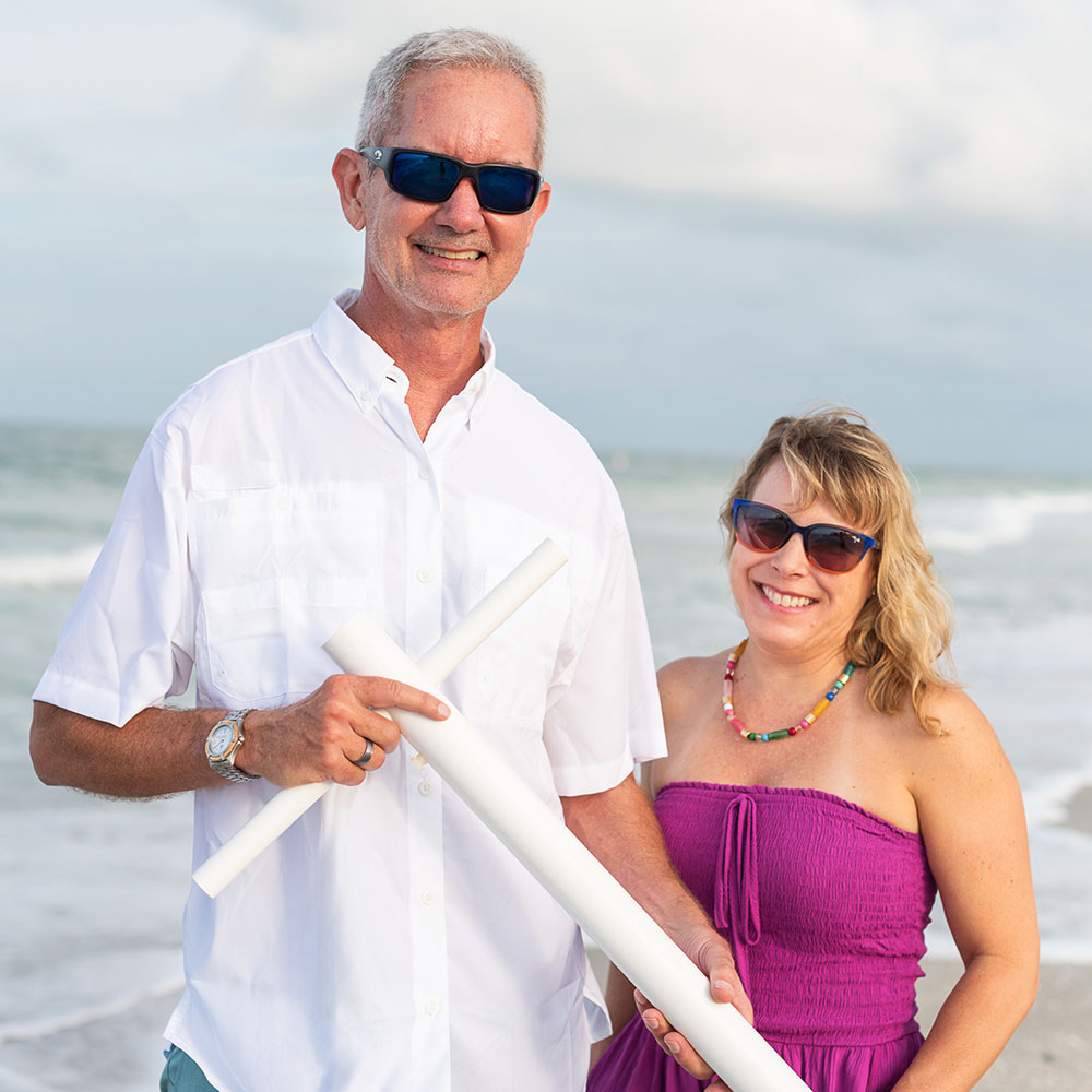 A headshot of the Suncoast Beach Shade co-founders, Mike & Hope, smiling on the beach while Mike holds the beach anchor in front of them