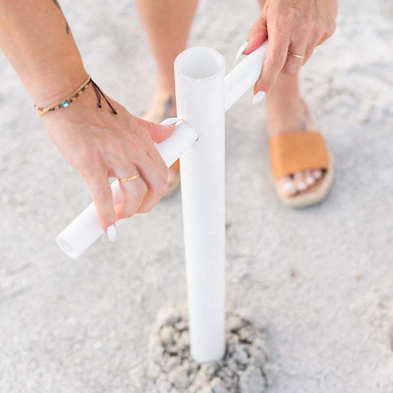 A close up of a woman on the beach setting up the Suncoast Beach Shade umbrella anchor by screwing it into the sand